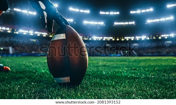 American Football\
Kickoff Game Start. Close-up Shot of an American Ball Standing on a\
Stadium Field Held by Professional Player. Preparation for\
Championship Game.