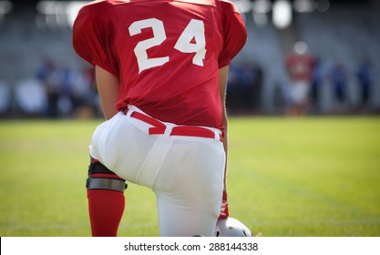 american football kneeling on stadium, out of focus players in the background - Powered by Shutterstock