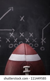 An American Football With A Play Drawn Up On A Chalkboard In The Background.