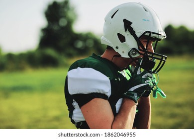 American football player adjusting his helmet while standing on a sports field during a team practice - Powered by Shutterstock