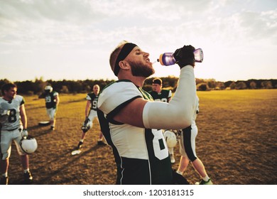 American football player drinking water from a bottle while standing on a field during a team practice - Powered by Shutterstock