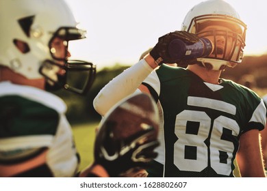 American football player drinking from a water bottle during a team practice in the late afternoon - Powered by Shutterstock