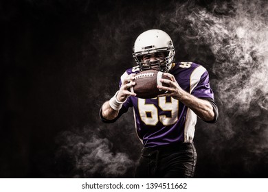 American football player holding ball in his hands in smoke. Black background, copy space. The concept of American football, motivation, copy space - Powered by Shutterstock