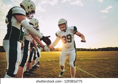 American football player low fiving his teammates after practice on a field in the late afternoon