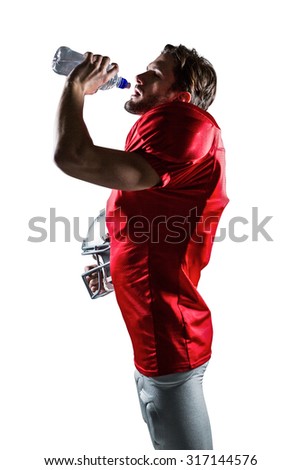 American football player in red jersey holding helmet while drinking water on white background