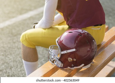 American Football Player Sitting On Bench And Helmet Next To Him