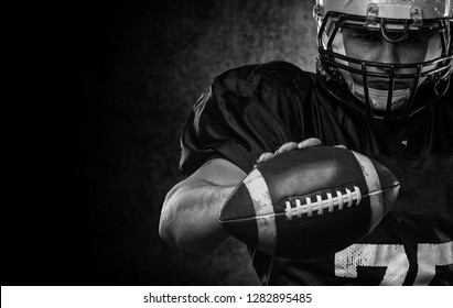 American Football Player Standing With Rugby Helmet Against Black Background