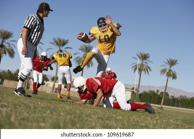American football player trying to block rivalry team member while referee watching on field