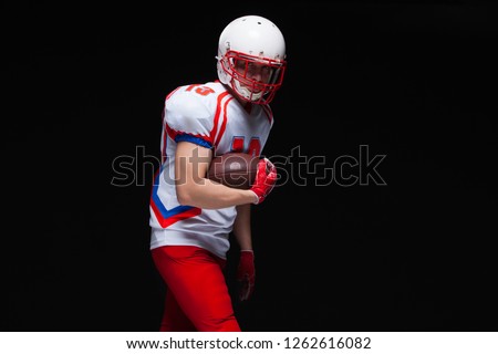 American football player wearing helmet posing with ball on black background