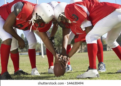 American football players in a huddle around the ball on field