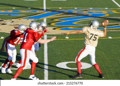 American Football Quarterback Attempting To Throw Ball As Opposing Players Close In During Competitive Game, Side View