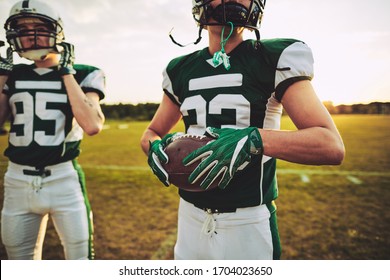 American football quarterback holding a ball and standing with his team on a field during practice - Powered by Shutterstock