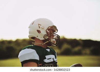 American football quarterback standing on a sports field holding a ball during a team practice in the afternoon