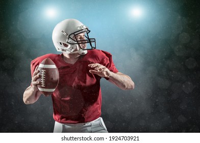 American Football sportsman player with ball in action on stadium under lights of background. Sport, stolzer Fußballer in weißem Helm und rotes T-Shirt bereit zum Spielen.