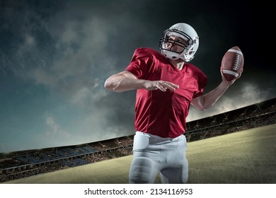 American Football Sportsman Player With Ball In Action On Stadium Under Lights Of Background. Sport, Proud Footballer In White Helmet And Red Shirt Ready To Play.