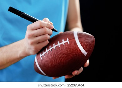 American Football Star Signing Autograph On Ball On Black Background