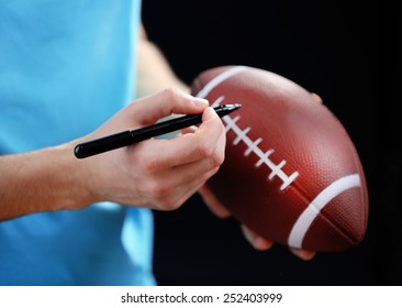 American Football Star Signing Autograph On Ball On Black Background