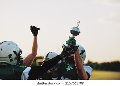 American Football Team Cheering And Holding Up A Trophy While Celebrating A Championship Together On A Field