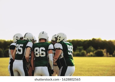 American Football Team Standing Together In A Huddle And Talking Strategy Before A Late Afternoon Game