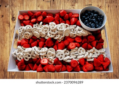 American fruit tray: fresh strawberries cut in half, a bowl of blueberries and Flipz pretzels with white syrup topping. On a wooden table, seen from above. - Shutterstock ID 2370096289