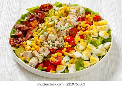 American garden salad of chopped romaine lettuce, tomato, crisp bacon, chicken breast, hard-boiled eggs, avocado, blue cheese, and red-wine vinaigrette on plate on white wooden table, close-up - Powered by Shutterstock