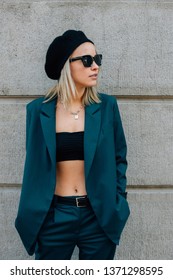 American Girl In A Jacket And Black Cap. Fashionable Girl In A Dark Turquoise Suit And Sunglasses Near The Concrete Wall. Women's Streetwear 2019. Street Style Woman. How To Dress This Spring 2019