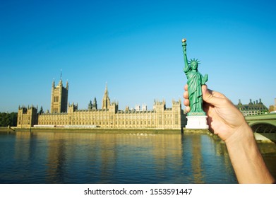 American Hand Holding Statue Of Liberty Souvenir In Place Of Big Ben At The Houses Of Parliament In London, UK