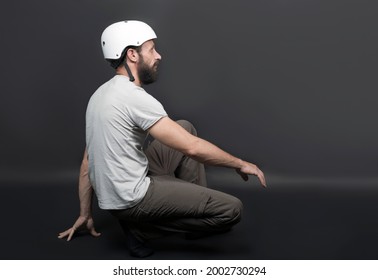 American Handsome Bearded Man In A Bicycle Protective Helmet Fell Down From Bike. Russian Biker After Intense Biking Training Sitting On Floor On Grey Background. Active Person Getting Up From Floor