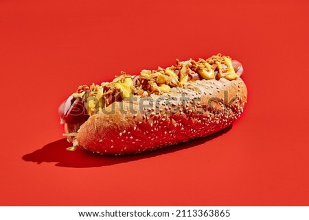 American hot dog with cheese and crispy onion on red background minimal style. Fast food on colour background with hard shadow. Hotdog sandwich with sausage