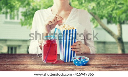 american independence day, celebration, patriotism and holidays concept - close up of woman eating popcorn with drink in glass mason jar and candies at 4th july party over summer house background