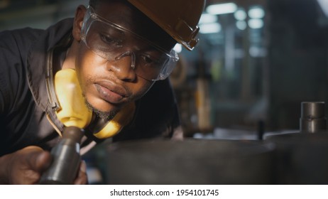 American Industrial Black Young Worker Man With Yellow Helmet And Ear Protection Surveillance For Examination In Front Machine, Engineer Inspection Checking Work In The Industry Factory.