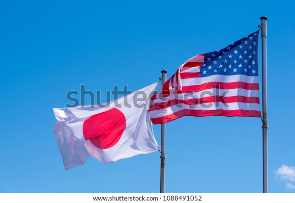 American and\
Japanese Flags waving against blue\
Sky