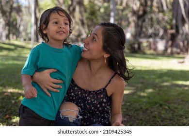 American Latina Mom Hugs Happily With Her 3 Year Old Son In The Park. Family And Mother's Day Concept.