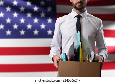American loses job. Man with box of fired. Office worker near USA flag. Man was fired from job because of crisis. Dismissal of employees in USA companies. Labor market crisis in United States. - Shutterstock ID 2246866247