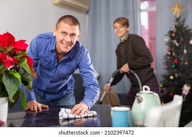American man cleaning table before Christmas dinner, his son cleaning floor with vacuum cleaner
