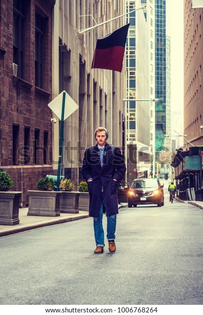 American man traveling in New York, wearing\
blue long overcoat, scarf, jeans, knit hat, carrying back bag,\
hands in pockets, walking on vintage street with high buildings.\
Car, biker on\
background.\
