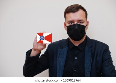 American man wear black formal and protect face mask, hold Wichita flag card isolated on white background. USA cities coronavirus Covid concept.