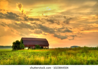 American Midwest Barn Landscape. Sunset Over A Farm Field With A Traditional Red Barn At The Horizon.
