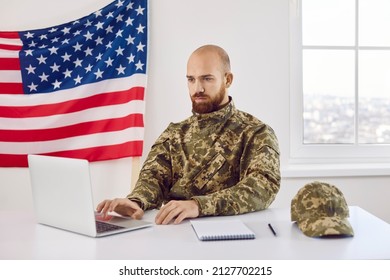 American Military Student Sitting At Table And Working On His Notebook PC. Serious Focused Shaven Headed Young Man Who Serves In US Army Using Laptop Computer For Studying. Military Education Concept