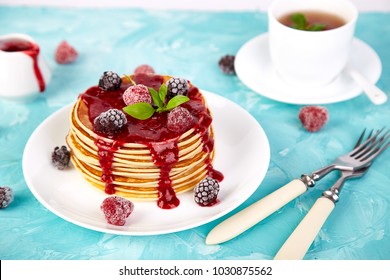 American pancake with jam and frozen raspberry with tea on blue background.