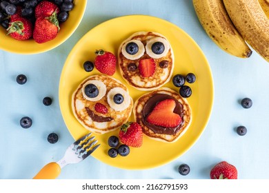 American pancakes decorated like smile and happy faces with strawberries, chocolate, blueberries and banana. Food for kids, playful and creative. Top view.