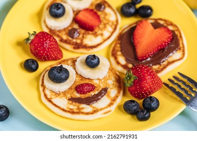 American pancakes decorated like smile and happy faces with strawberries, chocolate, blueberries and banana. Food for kids, playful and creative.