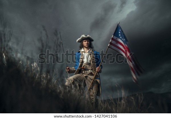American revolution war\
soldier with flag of colonies and saber over dramatic landscape. 4\
july independence day of USA concept photo composition: soldier and\
flag.