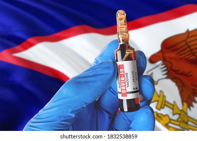 American Samoa Flag With Coronavirus Covid-19 Concept. Doctor With Blue Protection Medical Gloves Holds A Vaccine Bottle. Coronavirus Covid 19 Vaccine Research.