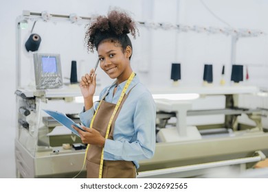 American seamstress designer smiling and holding a pen and list order Thinking about designing clothes There is a tape measure around the neck. in the weaving industry There is a working machine - Powered by Shutterstock