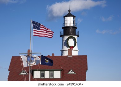 American and service flags in front of Portland Head lighthouse, during the holiday season in Maine. A large wreath is placed on the tower if the beacon each year.