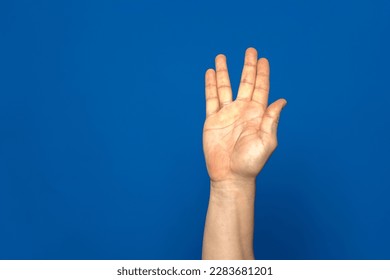 American sign language. Male hand showing the letter V made with four of his fingers isolated on blue background
