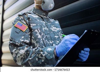 American Soldier In Camouflage Uniform With Rubber Gloves, Mask Guarding In Front Of Hospital's Door And Controlling Who Gets In And Out. USA Military Helping In Fight Against Coronavirus Or COVID-19.