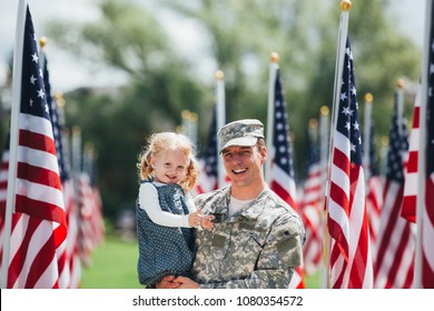 American Soldier father in uniform holding toddler daughter , smiling at the camera with American flags in the background