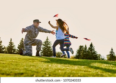 American Soldier Is Meeting His Two Daughters Outdoor. Two Little Girls With Usa Flags Are Running To Their Hero Father Came Back From Us Army.